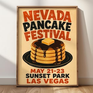 May include: A framed poster featuring a stack of pancakes topped with syrup and a butter pat on a black plate. The text reads NEVADA PANCAKE FESTIVAL, MAY 21-23, SUNSET PARK, LAS VEGAS. The design uses orange and black lettering on a cream background.