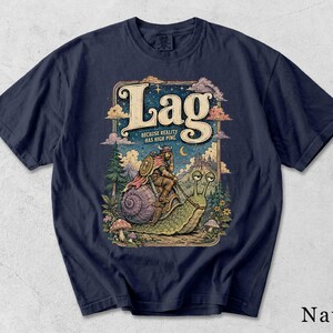 Könnte beinhalten: Ein marineblaues T-Shirt mit einer grafischen Illustration eines Wikingers, der auf einer riesigen Schnecke reitet. Der Text lautet "Lag" und "Because reality has high ping." Das Design zeigt einen Sternenhimmel, Berge, Kiefern und Pilze in einem Rahmen.