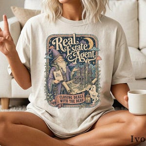 Könnte beinhalten: Ein elfenbeinfarbenes Kurzarm-T-Shirt mit einem Grafikdruck eines Zauberers, der einen Hausplan und einen Schlüsselbund hält. Der Text lautet Real Estate Agent und Closing Deals With The Dead, ergänzt durch ein Gespenst und ein Herrenhaus.