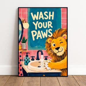 May include: A framed wall art print featuring a cartoon lion washing its paws in a bathroom sink. The illustration includes a mirror, a soap dispenser, a small plant, and a yellow rubber duck. The text reads WASH YOUR PAWS in large letters.