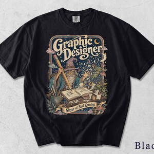 Könnte beinhalten: Ein marineblaues T-Shirt mit einer grafischen Illustration eines Zauberers, der einen großen Stift hält und in ein offenes Buch schreibt. Der Text "Graphic Designer" steht oben und "Slayer of Bad Kerning" auf einem Banner unten, umgeben von Sternen.