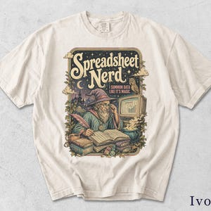 Könnte beinhalten: Ein elfenbeinfarbenes Kurzarm-T-Shirt mit einer Grafik eines Zauberers, der neben einem Computermonitor in ein Buch schreibt. Der Text lautet Spreadsheet Nerd und I SUMMON DATA LIKE IT'S MAGIC. Die Illustration zeigt Bücher, einen Kessel und eine Eule.