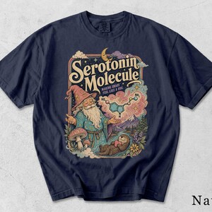 Może przedstawiać: Granatowy t-shirt z nadrukiem graficznym przedstawiającym czarodzieja z długą białą brodą, grzyba oraz wydrę trzymającą serce. Tekst głosi Serotonin Molecule oraz Making Chaos Feel Like A Hug, wraz z diagramem przedstawiającym strukturę chemiczną.