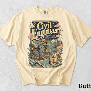 Op de afbeelding: Een boterkleurig t-shirt met een grafische illustratie van een civiel ingenieur die een landmeetkundig instrument gebruikt. Het ontwerp bevat de tekst "Civil Engineer I Turn Coffee Into Bridges", een dampende koffiemok, blauwdrukken en een brug.