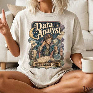 Könnte beinhalten: Ein elfenbeinfarbenes T-Shirt mit einer grafischen Illustration einer Person mit Brille, die eine Lupe hält, umgeben von Büchern, einer Kerze und einer Mondsichel. Der Text lautet Data Analyst und Making Numbers Confess im Vintage-Stil.