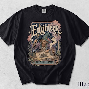 Könnte beinhalten: Ein schwarzes Kurzarm-T-Shirt mit einem Grafikdruck eines Zauberers mit Hut und Brille, der einen Schraubenschlüssel hält und an einem Bauplan arbeitet. Der Text "Engineer" und "BUILT ON BAD IDEAS" ist in einer dekorativen Schrift abgebildet.