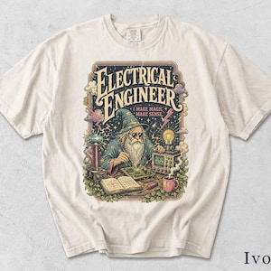 Könnte beinhalten: Ein elfenbeinfarbenes T-Shirt mit einer Grafik eines Zauberers mit sternenbesetztem Hut und Sonnenbrille, der eine Leiterplatte lötet. Der Text lautet "ELECTRICAL ENGINEER" und "I MAKE MAGIC MAKE SENSE", ergänzt durch eine Teslaspule und eine Glühbirne.