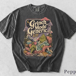 May include: A charcoal gray t-shirt featuring a graphic print of a green character in a robe sitting in a red armchair. The text reads Grinch Mode Generic, Not Today, Not Ever. The illustration includes a bowl of popcorn, a slice of pizza, and a remote.
