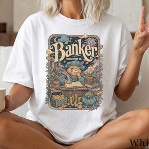 Könnte beinhalten: Ein weißes T-Shirt mit kurzen Ärmeln und einem farbenfrohen Grafikdruck eines Bibers als Bankier, der an einem Schreibtisch mit Büchern, Münzen und einer Schatztruhe sitzt. Der Text "Banker" und "Coins never lie" ist über dem Motiv abgedruckt.