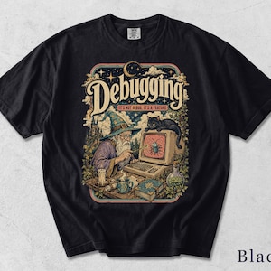 Puede incluir: Una camiseta de color marfil de manga corta con una ilustración gráfica de un mago ante un ordenador y un gato negro. El texto dice "DEBUGGING" y "IT'S NOT A BUG, IT'S A FEATURE." El diseño incluye una vela, un libro, una botella de poción y un castillo.