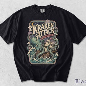 Könnte beinhalten: Ein schwarzes T-Shirt mit einer grafischen Illustration eines riesigen grünen Oktopus, der ein hölzernes Segelschiff inmitten von Meereswellen angreift. Der Text "KRAKEN ATTACK" und "SEA FOOD FIGHT BACK" steht über dem Motiv mit Mond und Sternen.