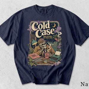 May include: A navy blue t-shirt featuring a graphic illustration of a skeleton detective wearing a deerstalker hat at a desk. The text reads Cold Case, Some Mysteries Just Need A Nap, and #1 Sleuth on a mug. Includes a typewriter, files, and a magnifying glass.