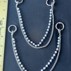 May include: Two silver-toned metal chains featuring white faux pearl beads, each attached to circular spring-gate rings. A yellow ruler is visible on the left, showing the larger chain spans approximately 8.5 inches in total length.