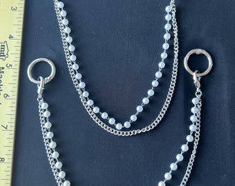 May include: Two silver-toned metal chains featuring white faux pearl beads, each attached to circular spring-gate rings. A yellow ruler is visible on the left, showing the larger chain spans approximately 8.5 inches in total length.