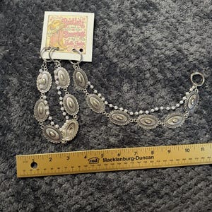 May include: A silver-toned boot chain accessory featuring oval concho-style medallions and small white beads, attached to a branded card labeled Bootlets and Bearings by Joelle Jaden. A yellow ruler shows the chain length is approximately 11 inches.