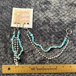 May include: A boot accessory set featuring two dangling strands of turquoise chips and white beads attached to silver-tone rings. The display card reads Bootlets and Bearings by Jodie Jaden. A yellow ruler shows the item length is approximately 8 inches.