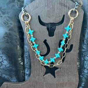 May include: A double-strand necklace featuring a gold-toned chain and a strand of bright turquoise cross-shaped beads interspersed with small gold-toned spherical beads. The necklace is secured with two circular gold-toned clasps at the ends.