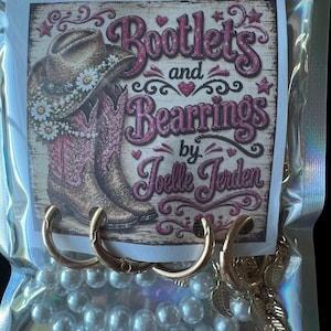 May include: A clear plastic bag containing jewelry, including gold-toned hoop earrings and a strand of white faux pearls. A printed card inside features a cowboy boot illustration with daisies and the text Bootlets and Bearrings by Joelle Jerden.
