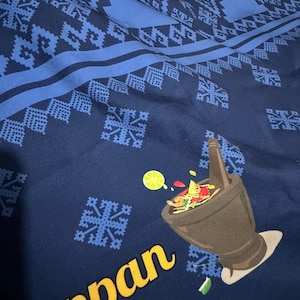 May include: A dark blue fabric featuring a repeating light blue geometric pattern and a graphic of a dark brown mortar and pestle filled with colorful ingredients, including a lime slice, with the yellow text "uppan" printed below the graphic.