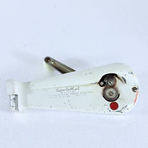 May include: A white manual Can-O-Mat can opener with a metal crank handle, a circular cutting mechanism, and a small red button. The body features printed text including Can-O-Mat, patent numbers, and Rival Mfg Co. Kansas City, Mo.