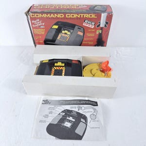May include: A North Coast Rocketry Command Control launch controller set in its original box. The set includes a black handheld controller with yellow and orange accents, a yellow circular safety key, and a printed instruction manual with diagrams.
