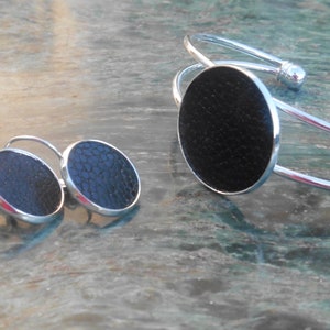 Könnte beinhalten: Ein Set aus silbernem Schmuck mit schwarzen runden Akzenten. Das Set enthält ein Armband und ein Paar Ohrringe.