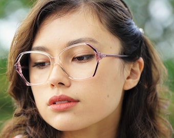 May include: A woman with long brown hair wearing clear pink-rimmed glasses. She is wearing a white shirt with red polka dots.