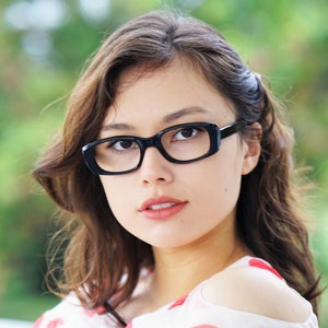 May include: A woman with dark brown hair wearing black framed glasses and a white and red polka dot shirt with one shoulder exposed.