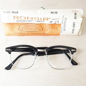 Puede incluir: Gafas negras y plateadas con montura superior negra y lentes transparentes. Las gafas están sobre una superficie clara, con un estuche vintage en el fondo. El estuche tiene el texto "Ronsir Browline Front".
