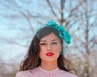 May include: A woman with long brown hair wearing a pink dress and a turquoise veil with a flower accent.