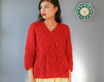 May include: A woman wearing a red cable knit sweater with a v-neck and a yellow skirt.