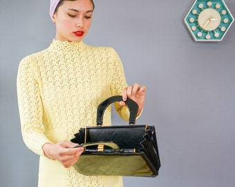 May include: A woman wearing a yellow crocheted dress and a pink headscarf holds a black vintage handbag with a gold clasp.