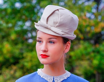 May include: A woman wearing a light beige hat with a bow and a blue sweater with a white lace collar.