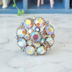 May include: A vintage brooch with a cluster of iridescent rhinestones in shades of blue, purple, and yellow. The rhinestones are set in a gold-toned metal.