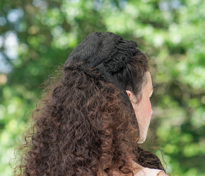 May include: A woman with long, curly brown hair wearing a black lace bonnet.