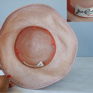 May include: A light pink straw hat with a wide brim and a smaller inner brim. The hat has a label that reads "Jack  Donnell Boutique".