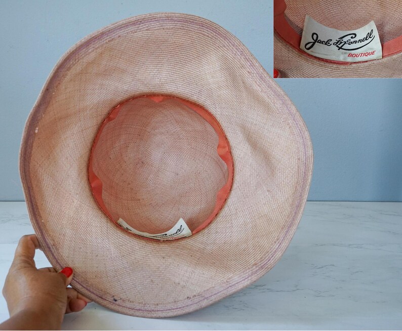 May include: A light pink straw hat with a wide brim and a smaller inner brim. The hat has a label that reads "Jack  Donnell Boutique".