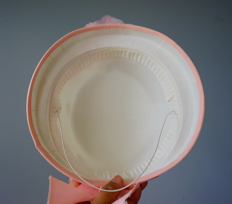 Op de afbeelding: Een roze hoed met een wit interieur en een draadframe. De hoed heeft een roze lint rond de basis.