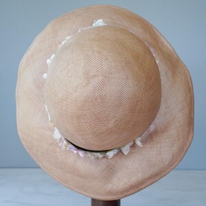 May include: A tan straw sun hat with a wide brim and a decorative trim of white and pink shells.