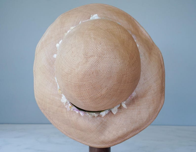 May include: A tan straw sun hat with a wide brim and a decorative trim of white and pink shells.