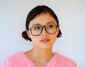 May include: A woman with dark brown hair wearing brown and black square-shaped glasses and a pink knitted jumper.