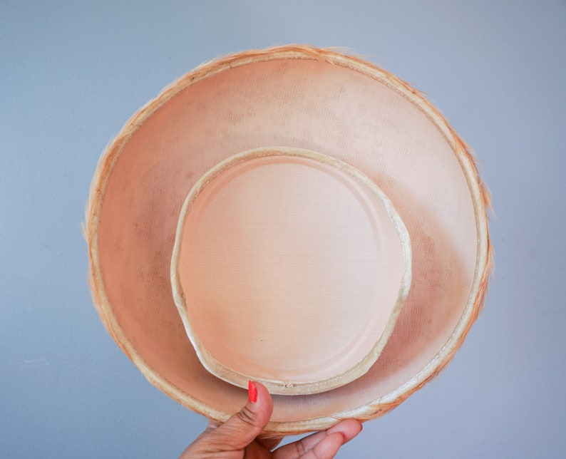 May include: A light pink hat with a wide brim and a smaller, inner hat. The hat is made of a woven material and has a soft, smooth texture.