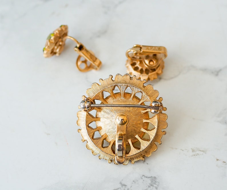 Peut inclure: Une broche dor&eacute;e avec un motif de filigrane et des strass verts. La broche a un fermoir &agrave; aiguille et un fermoir de s&eacute;curit&eacute;.
