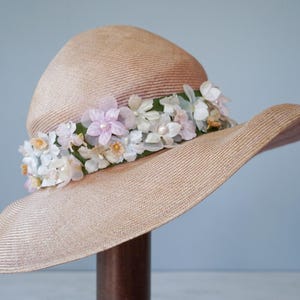 May include: A wide-brimmed straw hat with a pink and white floral trim. The hat is beige and has a woven texture.