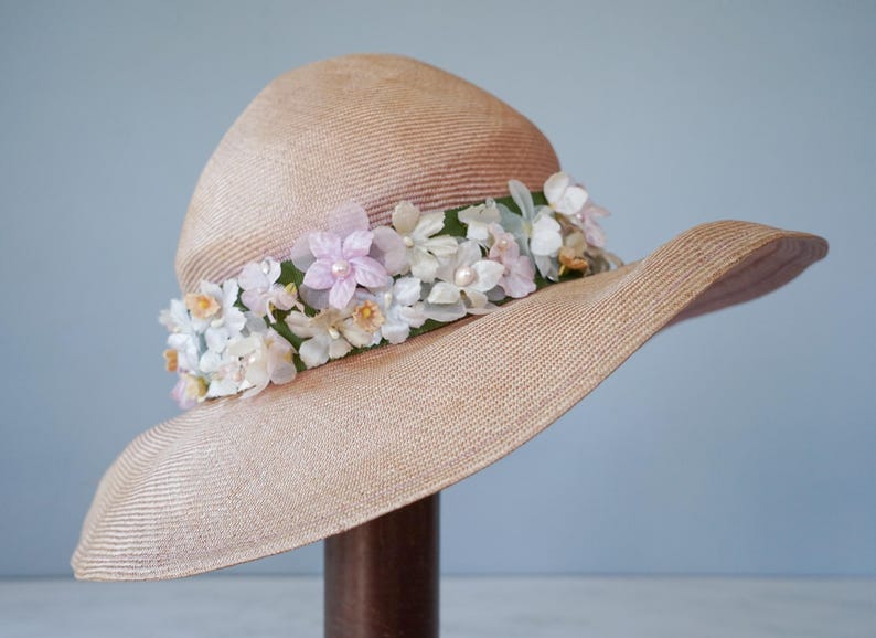May include: A wide-brimmed straw hat with a pink and white floral trim. The hat is beige and has a woven texture.