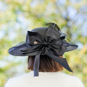 May include: A black hat with a large black bow and a small jeweled pin. The hat is made of straw and has a wide brim.