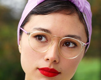 Könnte beinhalten: Eine Frau mit dunklen Haaren, die einen hellvioletten Turban und eine klare Brille trägt. Sie trägt ein gelbes Häkeltop und hat roten Lippenstift auf.