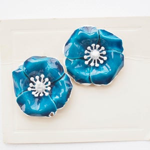 May include: A pair of blue enamel flower earrings with white centers. The flowers have a slightly textured surface.