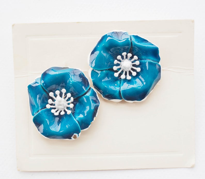 May include: A pair of blue enamel flower earrings with white centers. The flowers have a slightly textured surface.