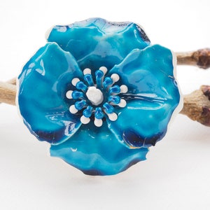 May include: A blue ceramic flower brooch with white and blue accents. The flower has a glossy finish and is shaped like a poppy.
